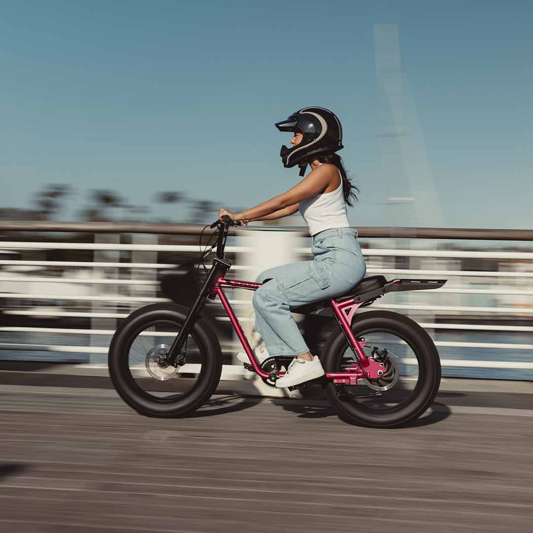 Young woman riding her SUPER73 ebike z miami in pink fast with a helmet on