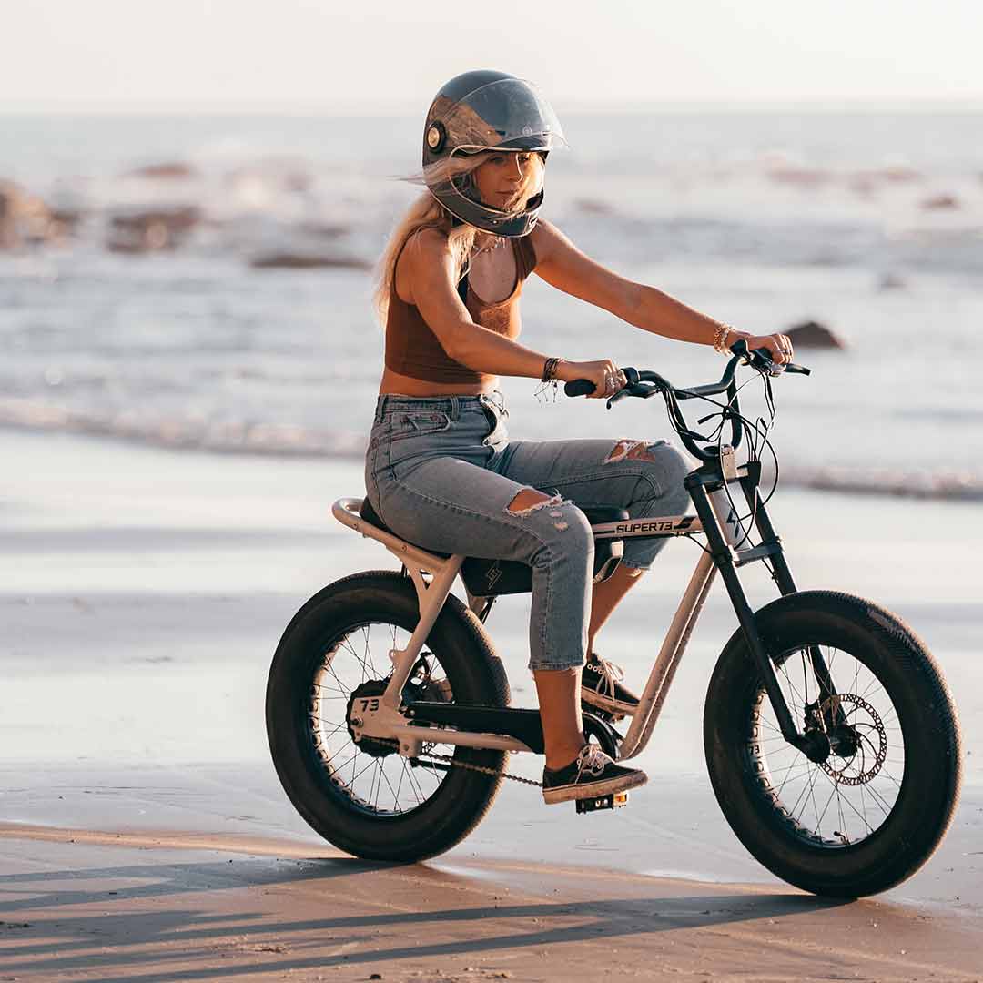 Young woman riding her super73 ebike z miami on the beach with a helmet on