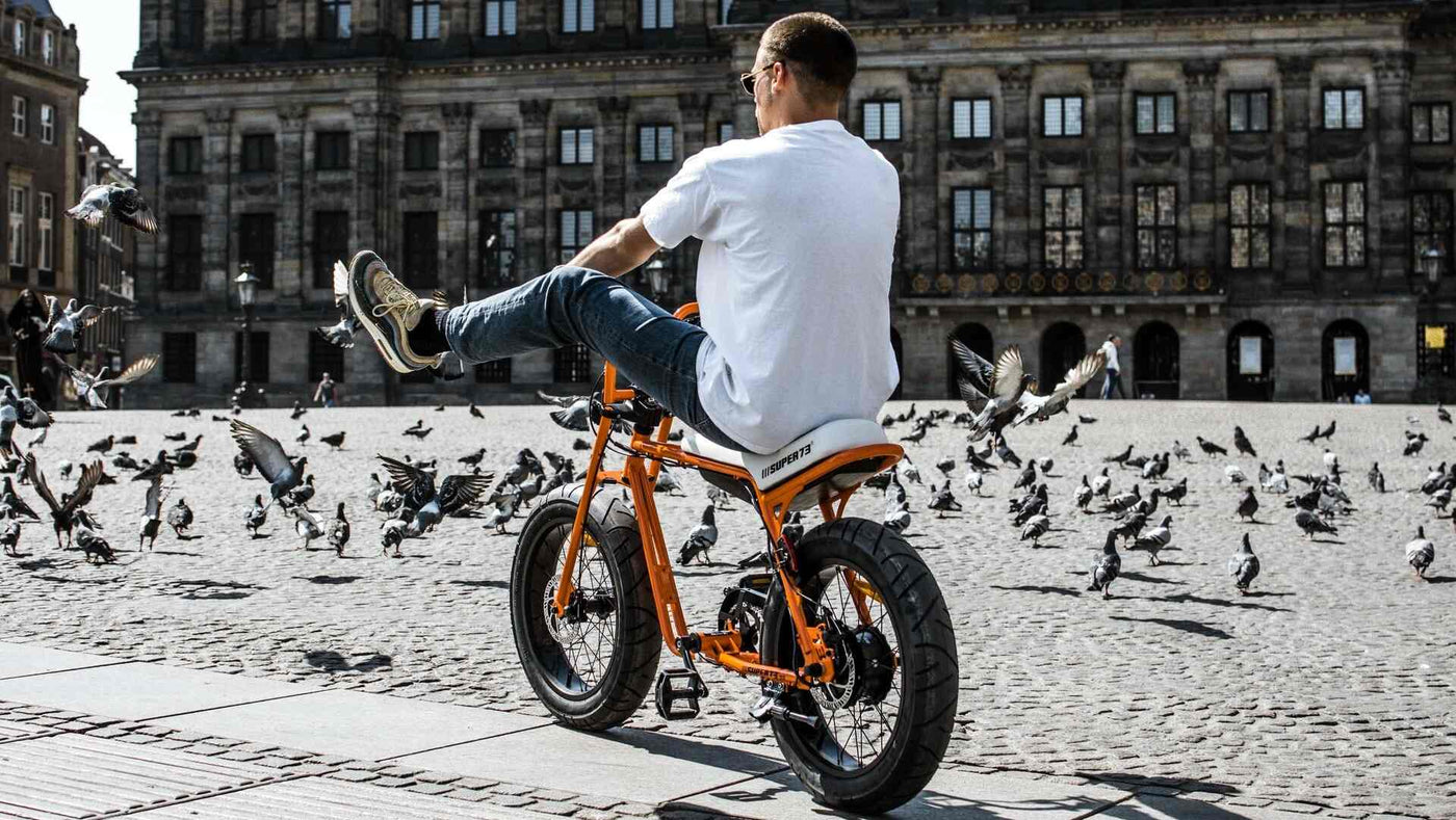 A man is riding a Super73-ZG Astro Orange in front of Dam Square in Amsterdam