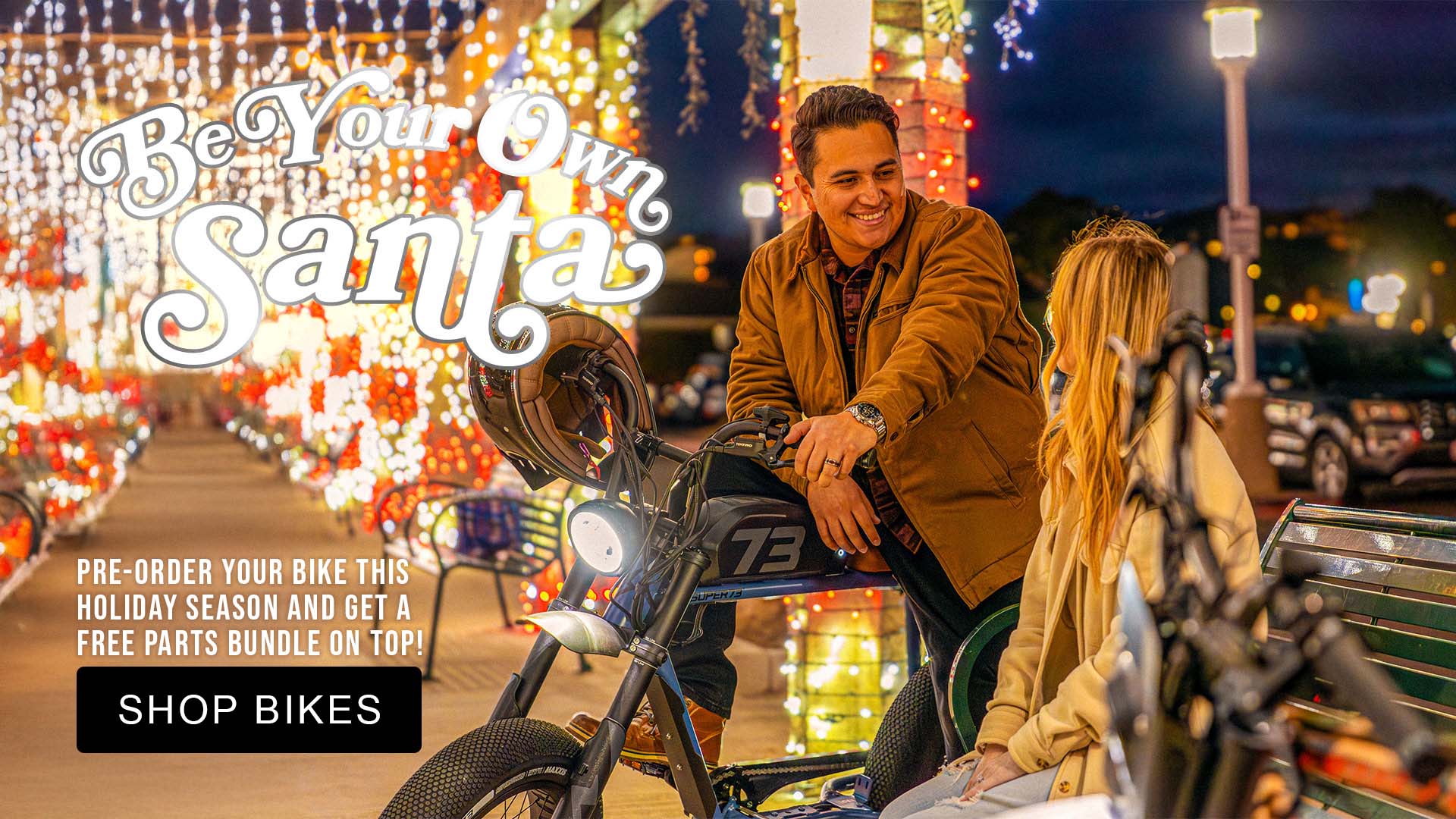 Man and woman on a super73 motorcycle with festive lights and 'Be Your Own Santa' text in the background.