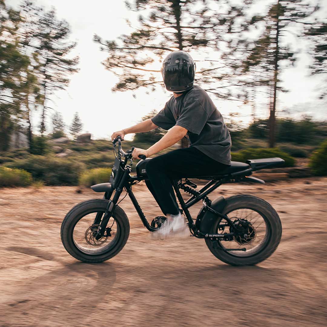 Helmeted rider on Super73 RX Mojave ebike looking at camera while riding on dirt road