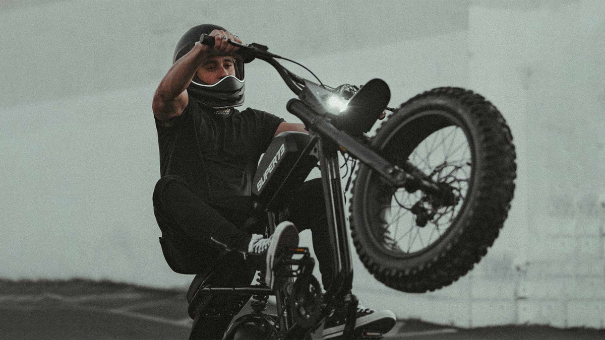 A young man popping a wheelie on a Super73 RX Mojave ebike featuring the suspension