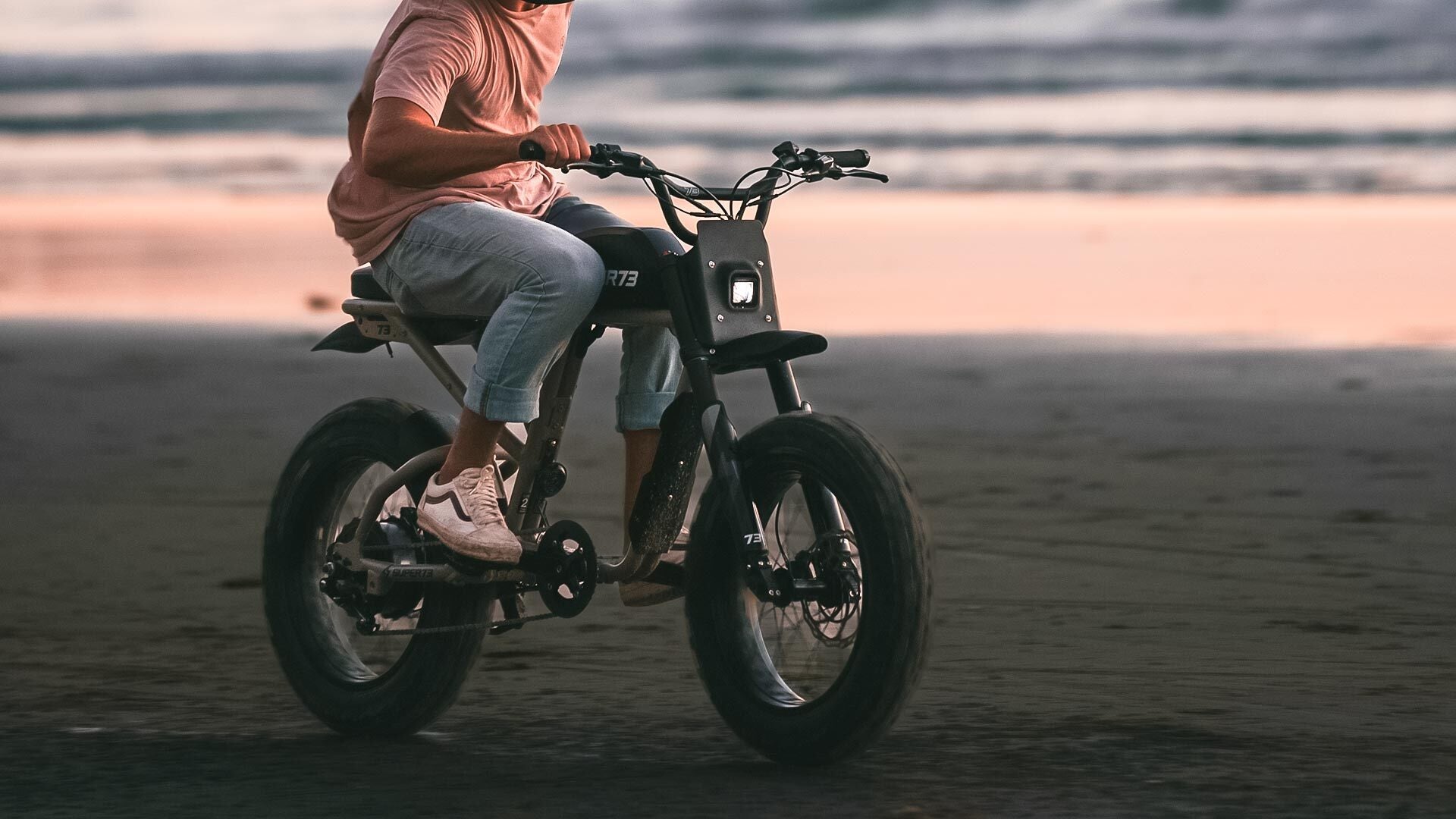 Rider on a Super73 ebike cruising along the sandy coast at sunset